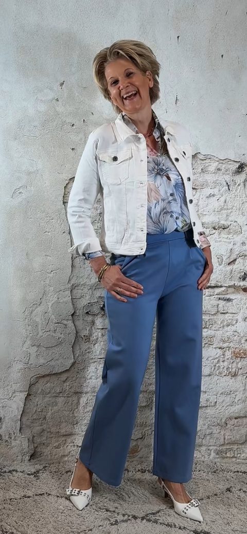 Luchtige bloemenblouse in jeansblauw met jeansblauw wijde pantalon en kort wit spijkerjasje, vrouwelijke look met hak.