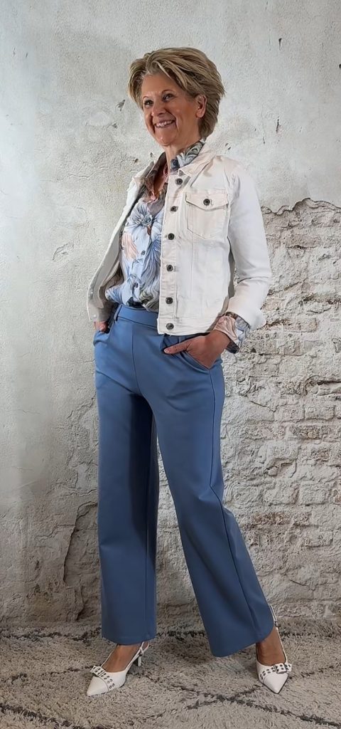 Luchtige bloemenblouse in jeansblauw met jeansblauw wijde pantalon en kort wit spijkerjasje, vrouwelijke look met hak.