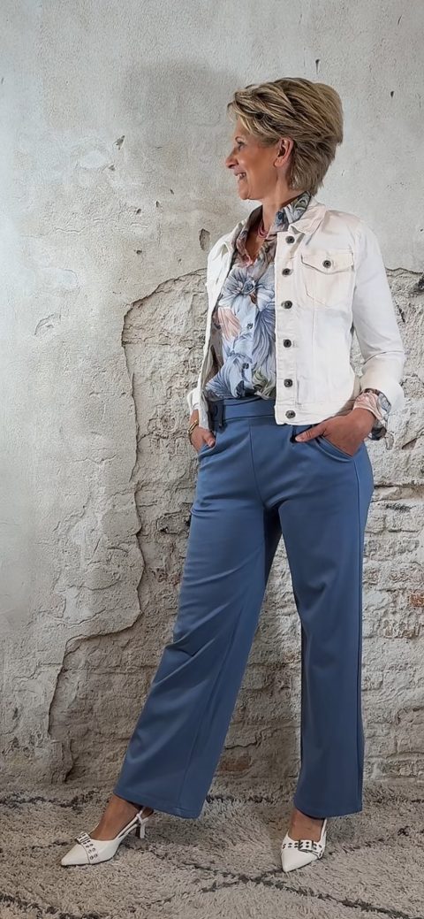 Luchtige bloemenblouse in jeansblauw met jeansblauw wijde pantalon en kort wit spijkerjasje, vrouwelijke look met hak.