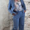 Transparante blouse met bloemenprint gestyled onder een blazer en semi-travelpantalon in jeansblauw, afgewerkt met witte hakken.