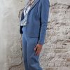 Transparante blouse met bloemenprint gestyled onder een blazer en semi-travelpantalon in jeansblauw, afgewerkt met witte hakken.
