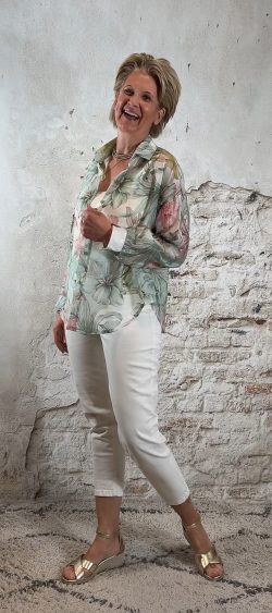Zijaanzicht van transparante lindegroene blouse met bloemenprint, gecombineerd met ecru jeans en gouden sandalen.