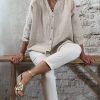 Linnen blouse zandkleur met opgerolde mouw, gecombineerd met ecru 3D-jeans en gouden sleehaksandaal – voorkant zittend