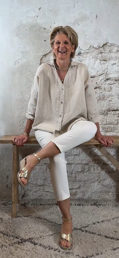 Linnen blouse zandkleur met opgerolde mouw, gecombineerd met ecru 3D-jeans en gouden sleehaksandaal – voorkant zittend